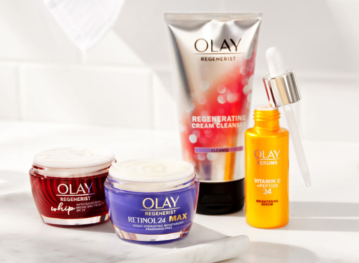 'The Day to Night' on a white, minimalist bathroom counter. The set features one Olay Regenerating Cream Cleanser, one Olay Vitamin C + Peptide 24 Brightening Serum, one jar of Olay Regenerist Whip moisturizer with SPF 25, and one jar of Olay Retinol24 MAX moisturizer.