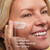 Model posing and smiling applying Collagen Peptide Moisturizing Cream to face. Lightweight. Deeply hydrating. Non greasy.