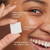 Model posing and smiling while holding melts cleanser swatch. Water activated daily facial cleanser. Dermatologist tested. Safe and effective for sensitive skin